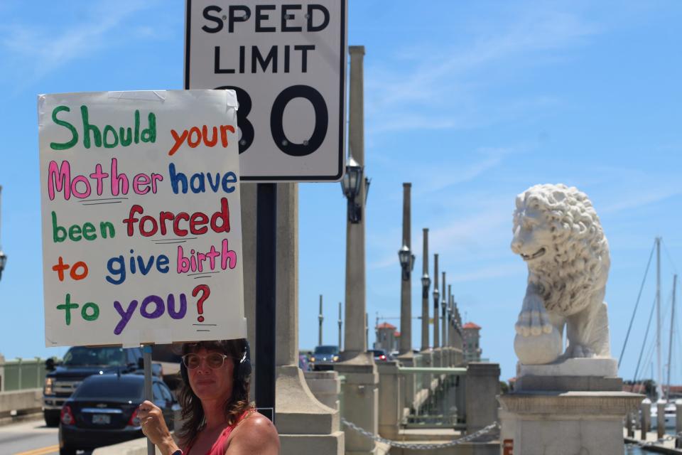 Marsha Turner stands at the base of the Bridge of Lions in St. Augustine, Florida on Saturday, May 14, 2022, holding a sign that reads: "Should your mother have been forced to give birth to you?"