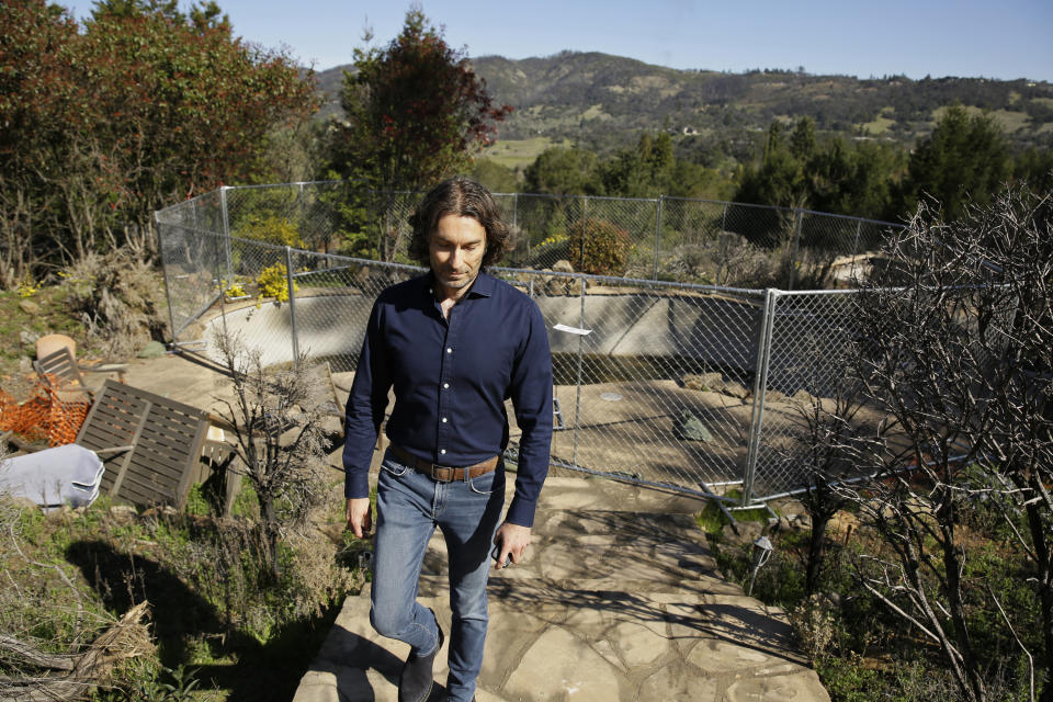 In this Tuesday, Feb. 25, 2020, photo, Jason Meek, whose Northern California wine country home was destroyed in 2017, walks through the remains of his home in Santa Rosa, Calif. A $13.5 billion settlement between victims, including Meek, of California's catastrophic wildfires and Pacific Gas & Electric was supposed to bring some peace and hope to people still reeling from the devastation. Instead, it has sparked confusion, resentment, suspicion and despair as the victims, government agencies, and lawyers grapple for their piece of the settlement fund. (AP Photo/Eric Risberg)