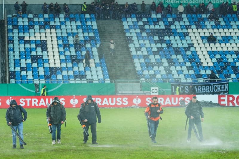 Workers try to remove puddles of water from the pitch before the German DFB Cup quarter final soccer match between 1. FC Saarbruecken and Borussia Moenchengladbach at Ludwigspark Stadium. A German Cup quarter-final between third division Saarbruecken and Borussia Moenchengladbach scheduled for later Wednesday is under threat because of a water-logged pitch. Uwe Anspach/dpa