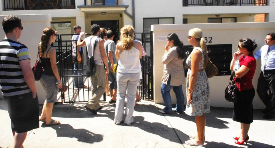 A dozen people line up outside a rental property in Queensland.