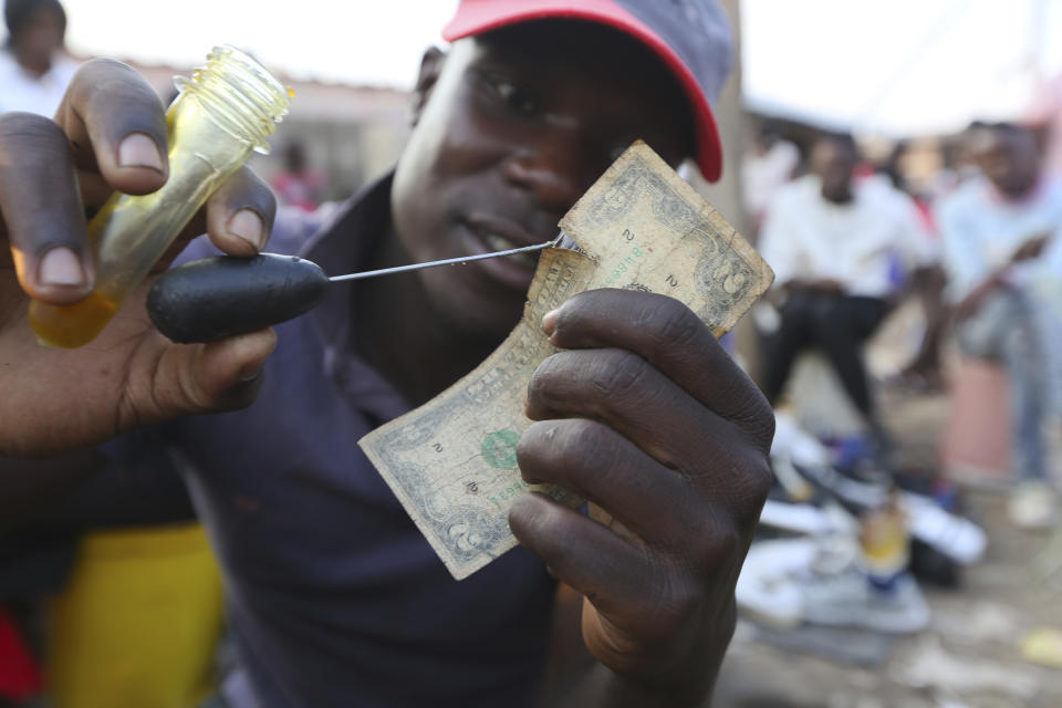 File - A currency trader mends an worn U.S. $2 bill at a market in Harare, Zimbabwe, on Oct, 26, 2020. Across the developing world, many countries are fed up with America’s dominance of the global financial system — and especially the power of the dollar. 80% of transactions in the Zinbabwe are in U.S. dollars. ( AP Photo/Tsvangirayi Mukwazhi, File)