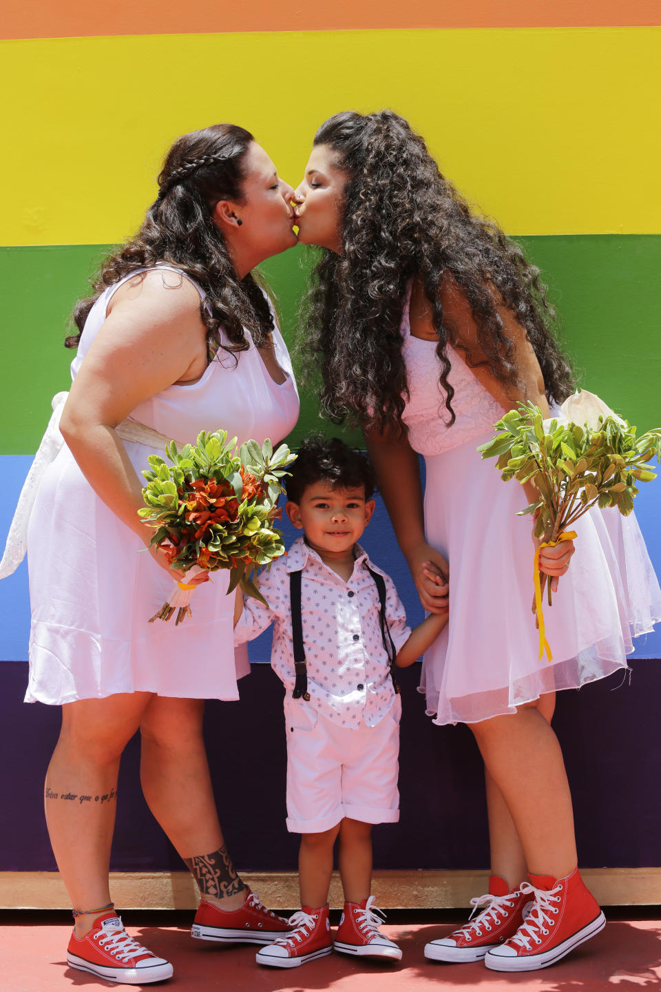 Newlyweds Thais Lococo Hansen, 32, left, and her partner Catarina Brainer, 28, share a kiss, as their son Pietro, 3, looks on during a group marriage of forty same sex couples in Sao Paulo, Brazil, on Saturday, Dec. 15, 2018. With the election of ultra-rightist Jair Bolsonaro as president, hundreds of same sex couples began to marry, fearing that the administration of Bolsonaro, who accumulates a history of homophobic and derogatory comments towards gays, could hinder the union of people of the same sex. (AP Photo/Nelson Antoine)