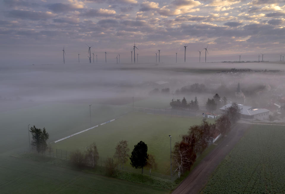 Fog floats over a soccer field in Stetten, Germany, March 19, 2024, backdropped by a wind energy plant. (AP Photo/Michael Probst, File)