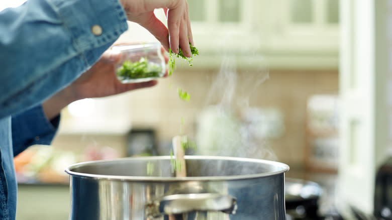 Person sprinkling herbs into pot