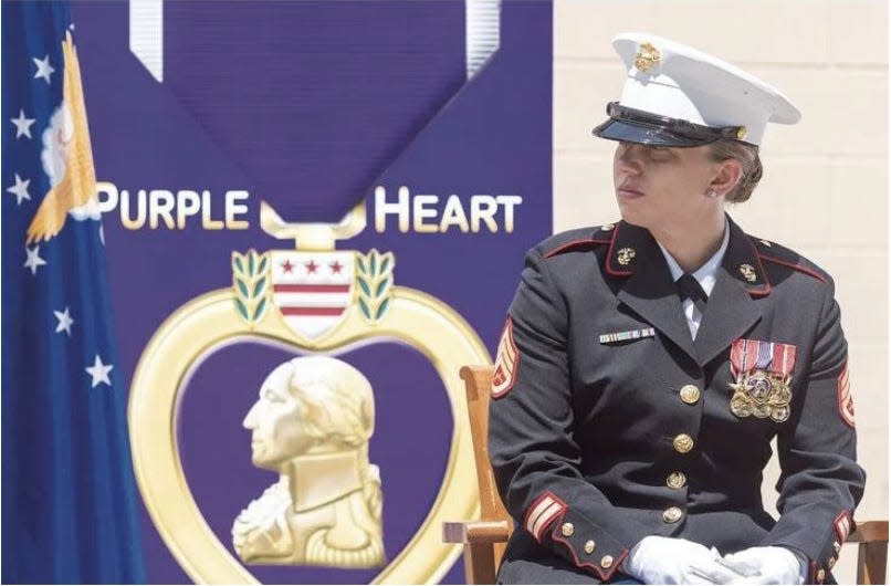 Sarah Cavanaugh sits in full Marine uniform in front of a Purple Heart Display
