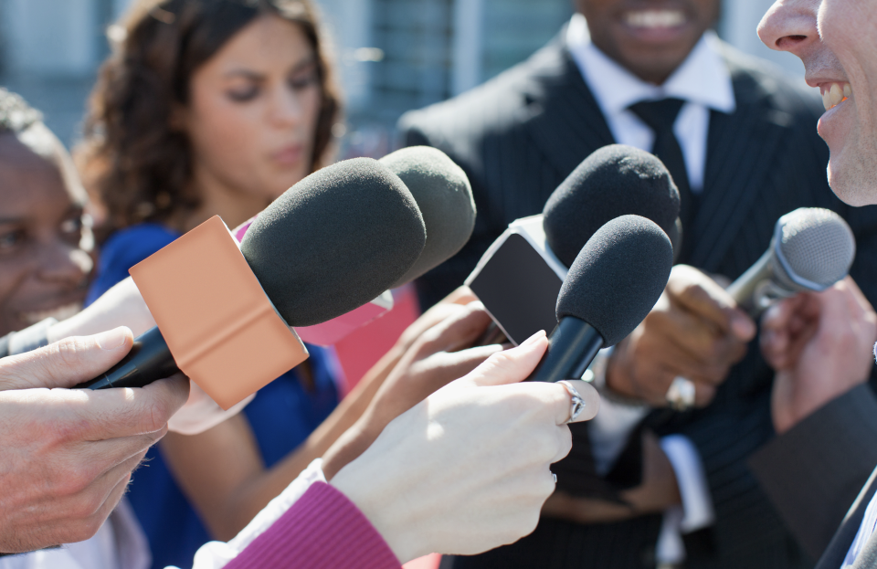 Person being interviewed by multiple reporters with microphones