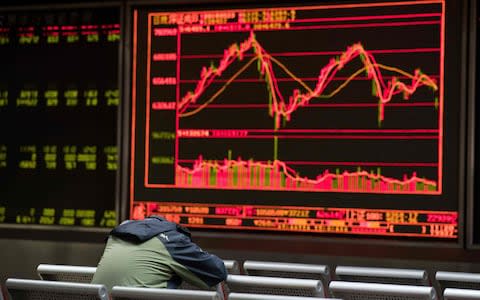 A man rests as he keeps an eye on stock price movements displayed on a screen at a securities company in Beijing - Credit: AFP