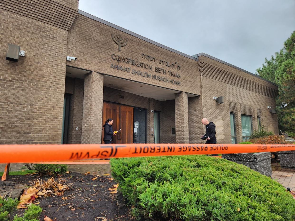 Police investigators examine the exterior of a synagogue in Dollard-des-Ormeaux, Que., where an incendiary device was ignited in November.  (Francois Joly/Radio-Canada - image credit)