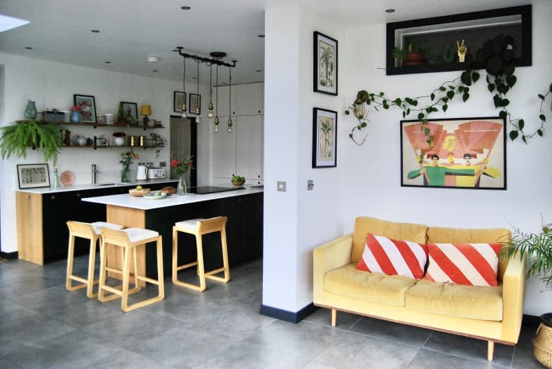 Kitchen with white countertops black cabinets and wooden accents next two a nook with a yellow couch and framed art.