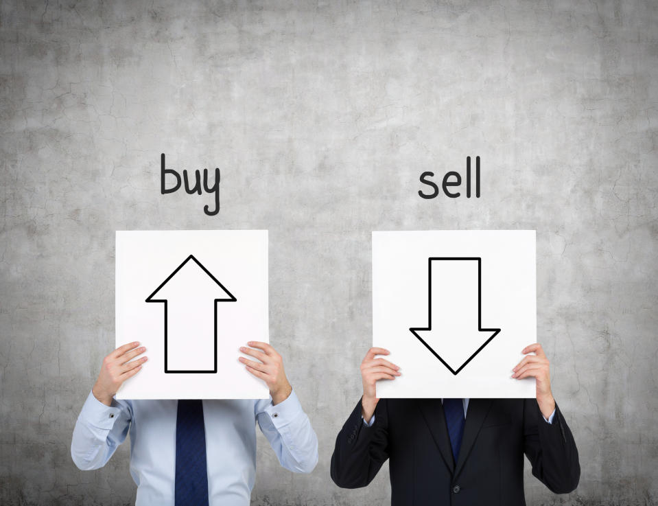 Two people holding signs with arrows pointing up and down with buy and sell written above them.