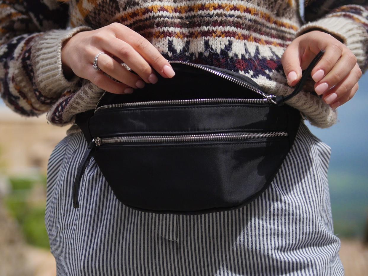 Woman wearing a colorful sweater and striped pants opening her black belt bag.