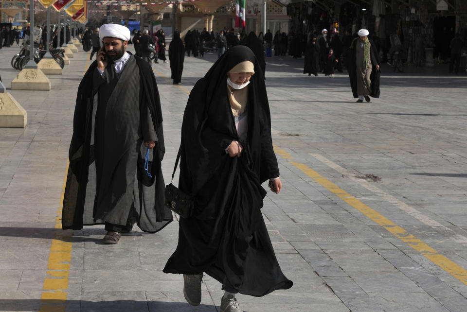 A woman and and clerics walk in front of the Fatima Masumeh Shrine at the city of Qom, some 80 miles (125 kilometers) south of the capital Tehran, Iran, Tuesday, Feb. 7, 2023. (AP Photo/Vahid Salemi)