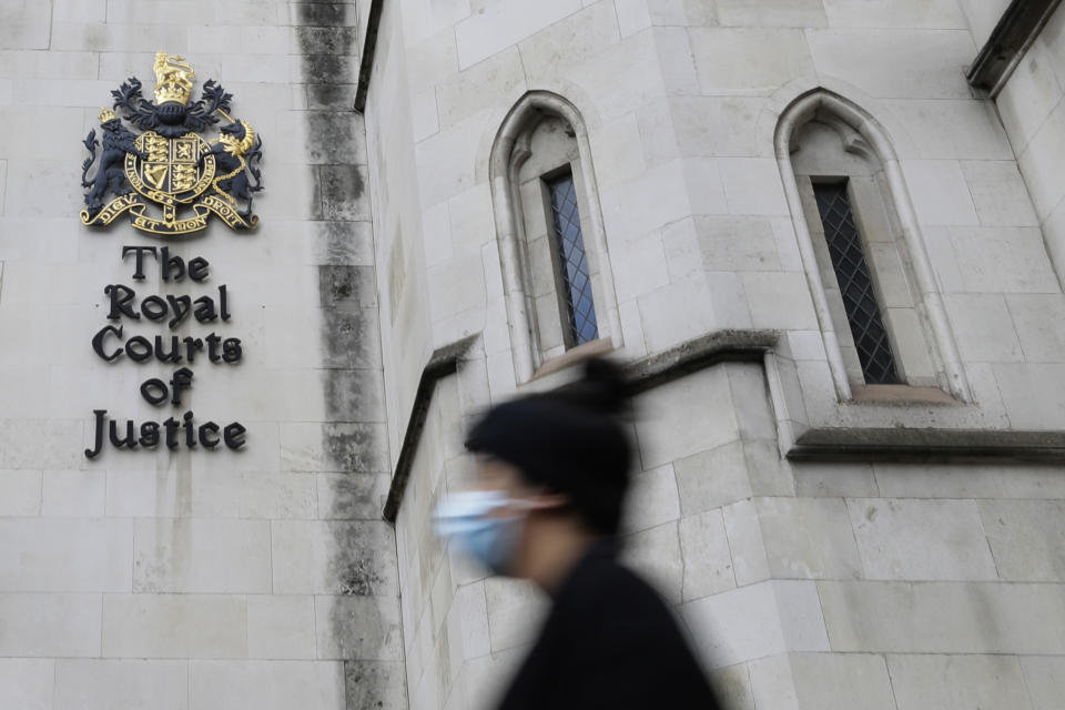 A pedestrian wears a mask as she passes by the Royal Courts Of Justice, in London, Tuesday, Jan. 19, 2021. Meghan, The Duchess of Sussex will ask a High Court judge to rule in her favour in her privacy action against the Mail on Sunday over the publication of a handwritten letter to her estranged father. The case will be heard remotely due to the pandemic. (AP Photo/Kirsty Wigglesworth)