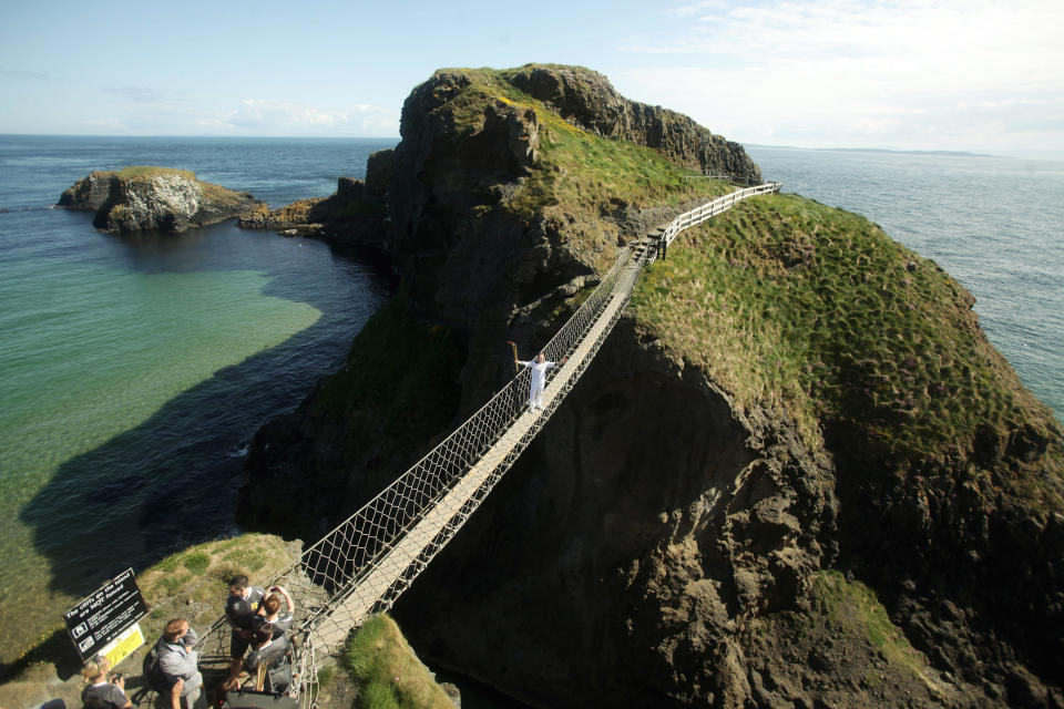 In this handout image provided by LOCOG, Torchbearer Denis Broderick holds the Olympic Flame on the Carrick-a-Rede rope bridge which links the mainland near the village of Ballintoy to the island of Carrickarede in County Antrim on day 17 of the London 2012 Olympic Torch Relay on June 4, 2012 near Belfast, Northern Ireland. The Olympic Flame is now on day 17 of a 70-day relay involving 8,000 torchbearers covering 8,000 miles. (Photo by LOCOG via Getty Images)