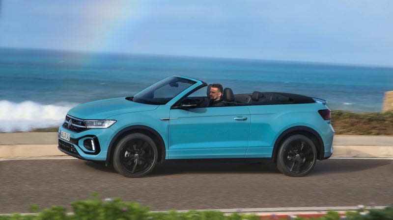 Front 3/4 view of a blue Volkswagen T-Roc Convertible driving along the coast