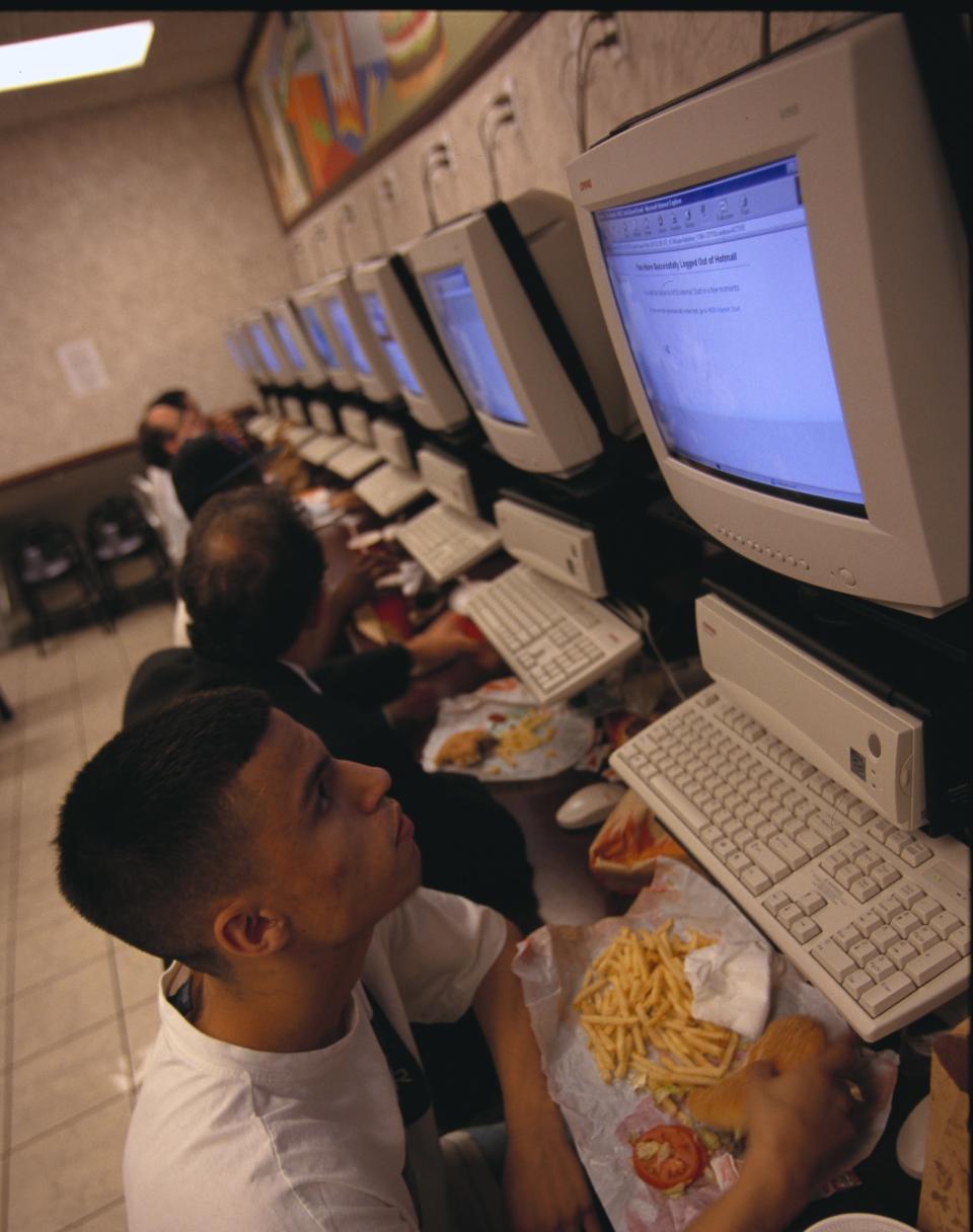 teen eating a burger and fries in front of a large 1990s desktop computer