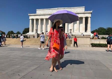 A tourist tries to shield herself from the sun using an umbrella in front of the Lincoln Memorial on a day when the temperature was forecast to reach 99 degrees F, in Washington