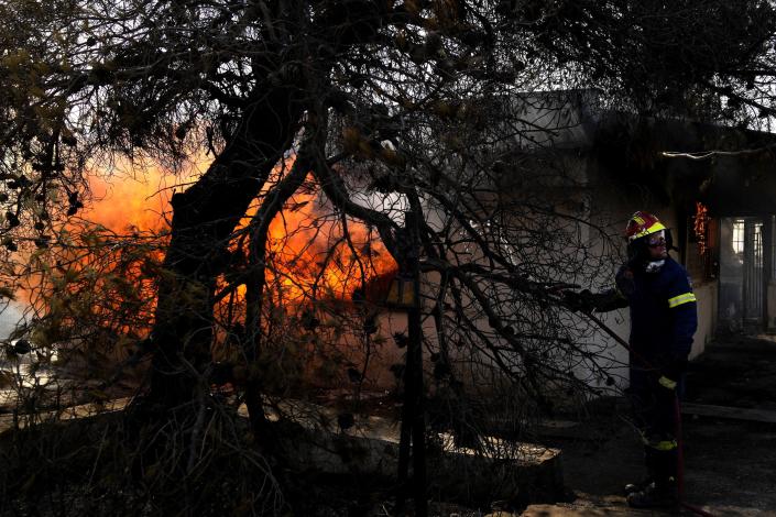 FILE - A firefighter tries to extinguish the fire in a house during a wildfire in Thea area some 60 kilometers (37 miles) northwest of Athens, Greece, Thursday, Aug. 19, 2021. In Greece, which suffered some of Europe's most devastating fires last August, authorities say higher fuel costs have added to challenges facing the Fire Service that relies heavily on water-dropping planes to battle blazes in the mountainous country. (AP Photo/Thanassis Stavrakis, File)