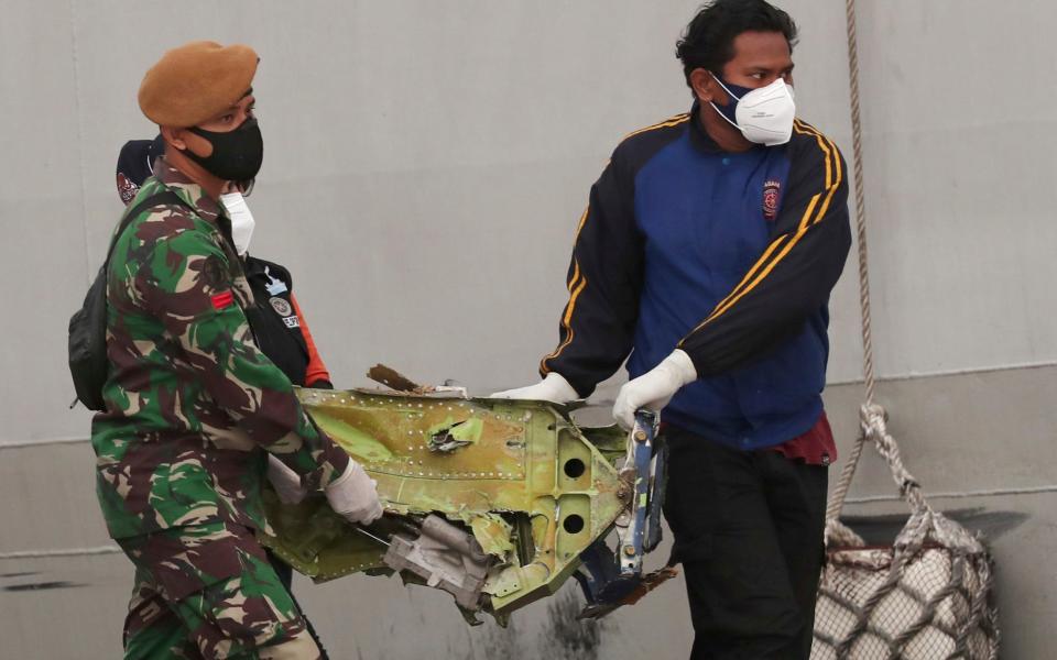 A soldier and rescuer carry debris found in the waters near the crash site - Tatan Syuflana/AP