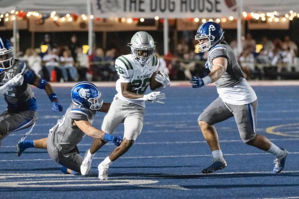 The De La Salle Spartans’ Anthony Dean (26) runs the ball for 14 yards before being tackled by the Folsom Bulldogs’ Daniel Chavez (10) in the first half of the game on Friday at Folsom High School.