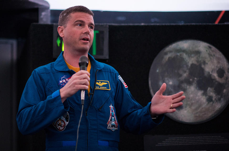 NASA astronaut Reid Wiseman at a 2015 public appearance in his hometown of Baltimore, Maryland, speaks in front of a photograph of the moon. As NASA's new Chief of the Astronaut Office, Wiseman may select the next crews to orbit and possibly land on the moon.