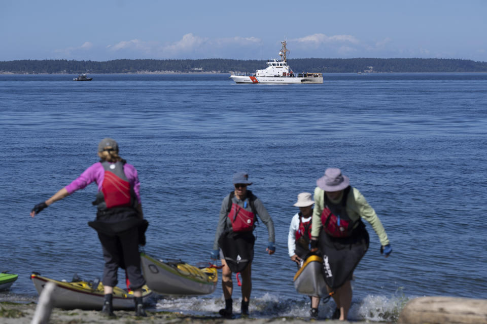 A U.S. Coast Guard boat searches the area Monday, Sept. 5, 2022, as kayakers pull out, near Freeland, Wash., on Whidbey Island north of Seattle where a chartered floatplane crashed the day before. The plane was carrying 10 people and was en route from Friday Harbor, Wash., to Renton, Wash. (AP Photo/Stephen Brashear)