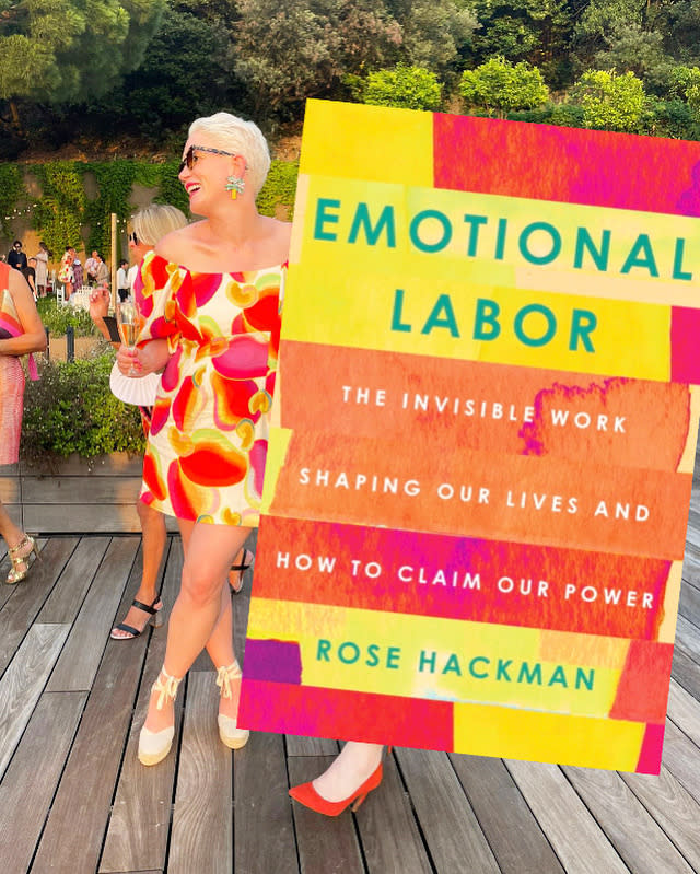 Rose, in a ruffled dress, stands next to a life-sized book cover of "Emotional Labor"