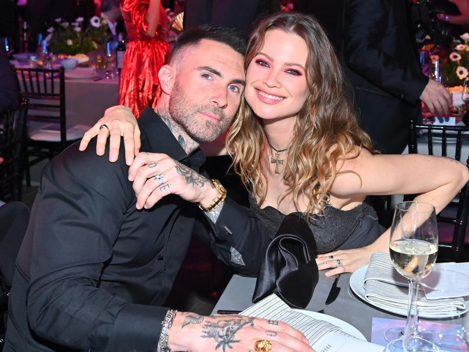 Adam in a black button down leaning into Behati smiling.