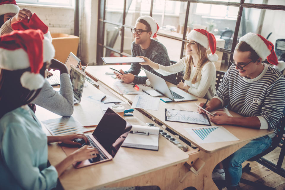 Merry Christmas and Happy New Year 2018!Multiracial young creative people are celebrating holiday in modern office. Group of young business people are sitting in Santa hats in last working day. Successful hipster team of freelancers.