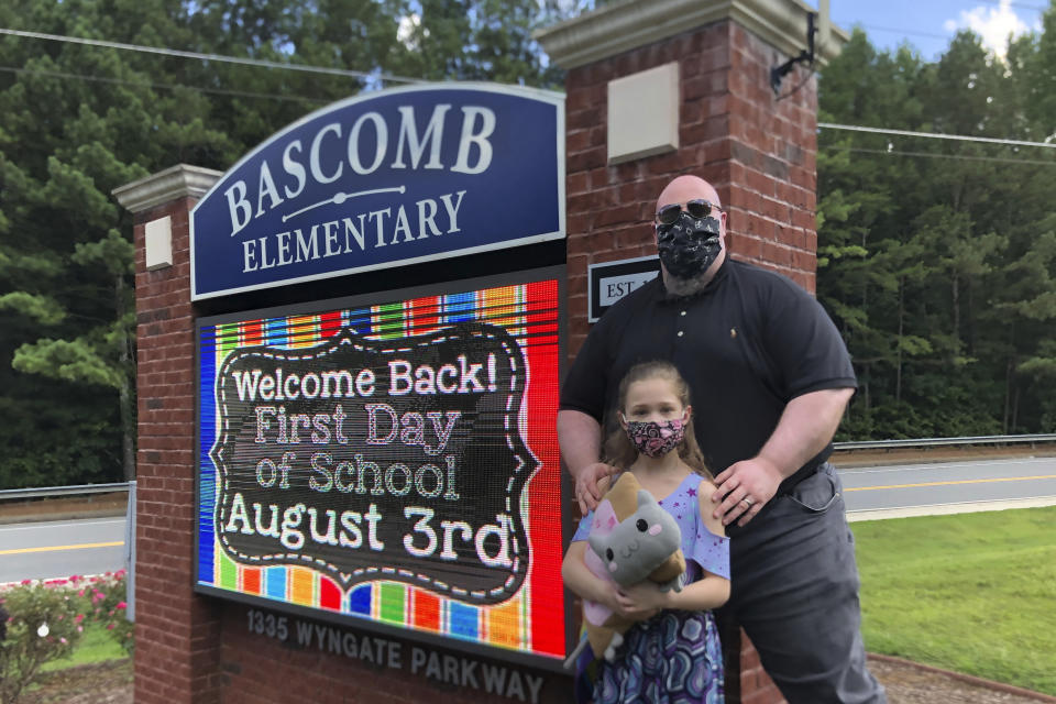 John Barrett and his daughter Autumn pose for photos outside Bascomb Elementary School in Woodstock, Ga., Thursday, July 23, 2020. Barrett says he will educate his daughter virtually and keep her out of in-person classes in Cherokee County schools, even though he's worried she will fall behind on her special education plans, because of concerns about COVID-19's spread. Cherokee County, near Atlanta, is one of many districts nationwide that gave parents a choice between in-person and all-online classes this fall. (AP Photo/Jeff Amy)