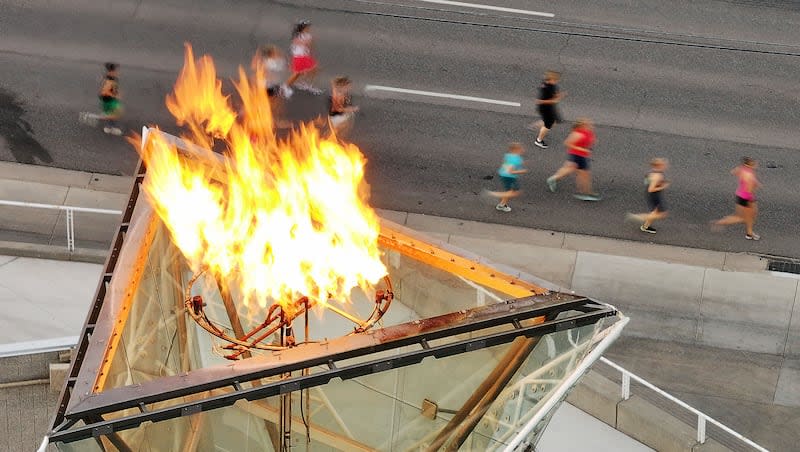 Deseret News racers run past the the Olympic Cauldron on Wednesday, July 24, 2024, in downtown Salt Lake City.