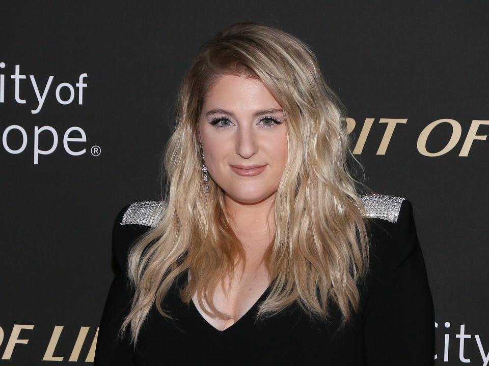 Singer Meghan Trainor wearing a black dress looking at the camera on a step-and-repeat