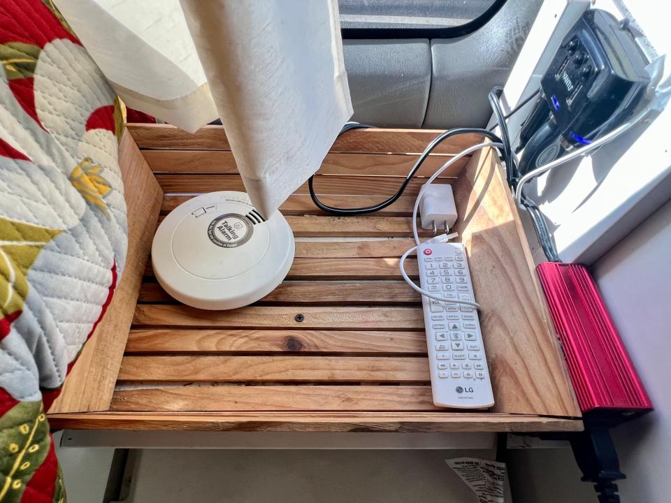 A wooden tray with a remote, fire alarm, and basic items in the van