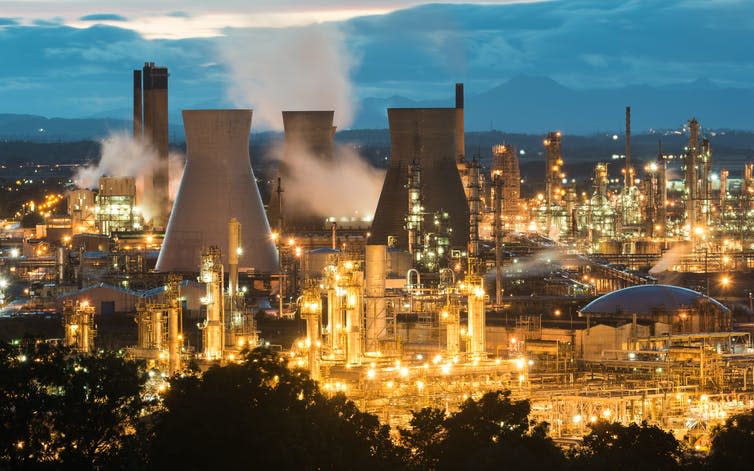 An industrial scene with three cooling towers and various chimneys lit up with yellow lights.