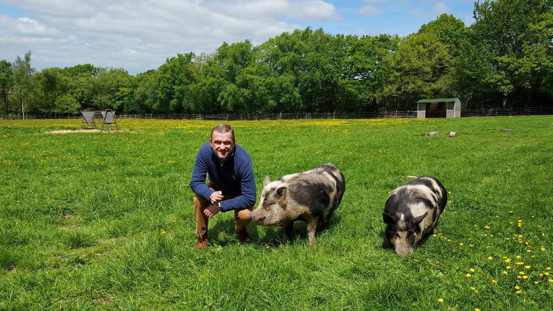 Kevan Hodges kneeling down beside two pigs in a field