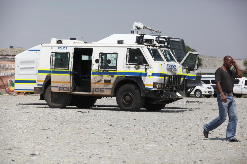 A man walks by a police vehicle stationed by a meeting of striking miners near Rustenburg, South Africa, on Wednesday, Nov. 14, 2012. Workers discussed a possible deal with Anglo American Platinum, or Amplats, on Wednesday as their weeks-long strike continued. Amplats is the world's top producer of platinum. (AP Photo/Jon Gambrell)