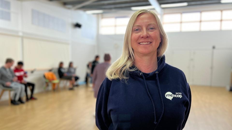 Ali Hand smiles at the camera as members of Jersey Mencap play boccia behind her