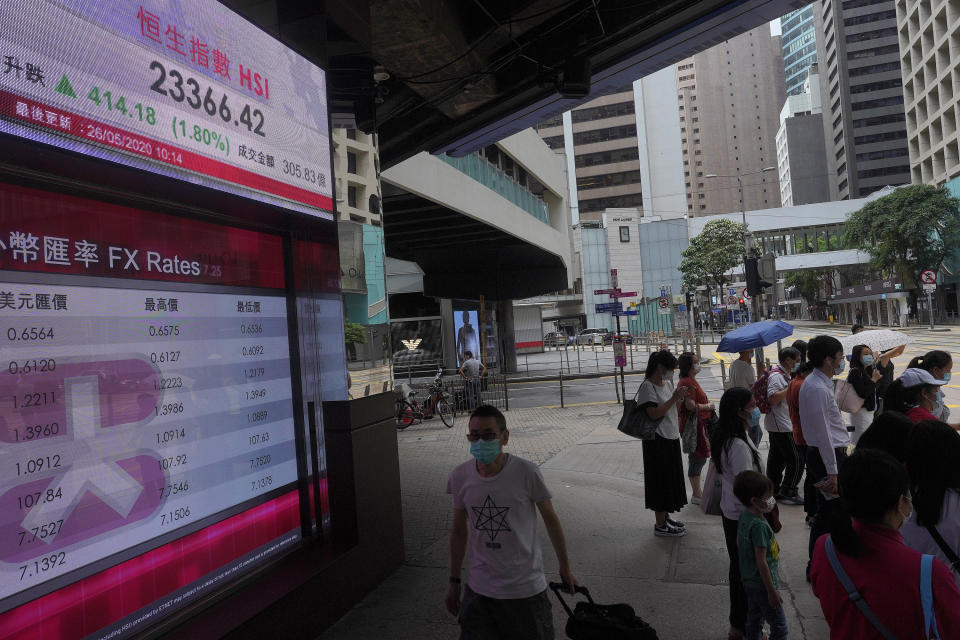 People wearing face masks stand near a bank electronic board showing the Hong Kong share index at Hong Kong Stock Exchange Tuesday, May 26, 2020. Asian shares are rising as some regions in Japan resume near-normal business activity, with hopes for economic recovery overshadowing worries over the coronavirus pandemic. (AP Photo/Vincent Yu)