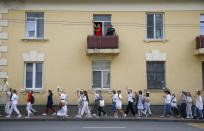 Belarusian women rally in solidarity with protesters injured in the latest rallies against the results of the country's presidential election while two men on a balcony greet them in Minsk, Belarus, Thursday, Aug. 13, 2020. Hundreds of people were back on the streets of Belarus' capital on Thursday morning, forming long "lines of solidarity" in protest against an election they say was rigged to extend the rule of the country's authoritarian leader and against a crackdown on rallies that followed the vote. (AP Photo/Sergei Grits)