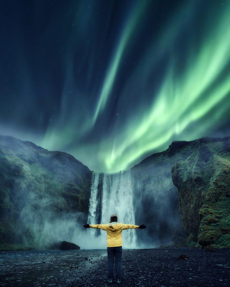 aurora borealis over skogafoss waterfall and cheerful tourist woman standing in travel famous place on summer in iceland