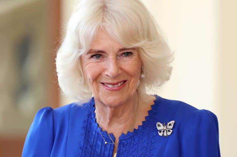 Camilla smiles at the camera in a dark blue dress