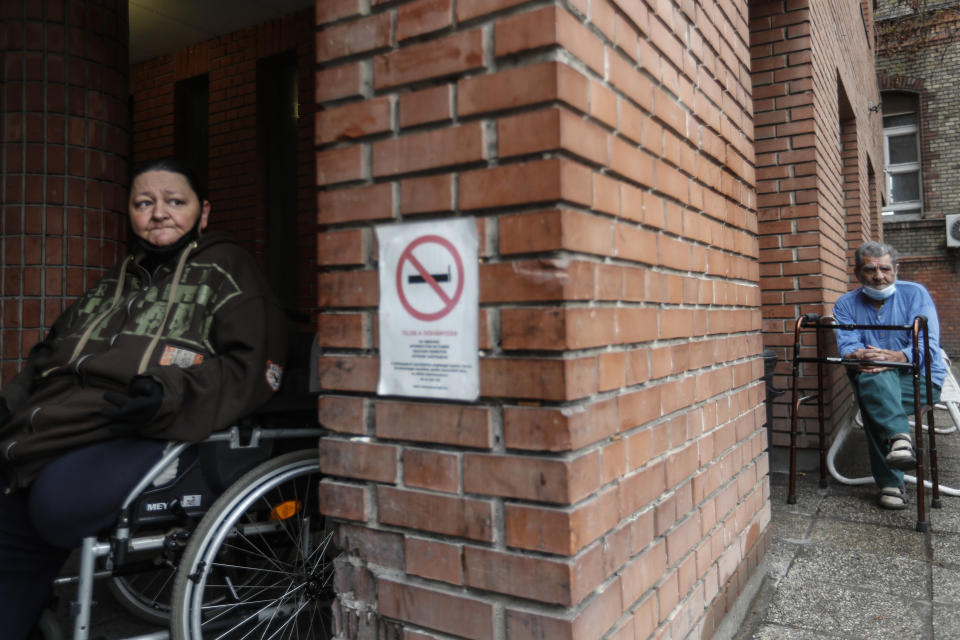 Patients sit outside the hospital for the homeless in Budapest, Hungary, Wednesday, April 14, 2021. A bitter conflict has emerged between Hungary’s right-wing government and the liberal leadership of the country's capital city over a hospital for the homeless that may soon have to close. The Budapest hospital provides medical and social services and shelter to more than 1,000 people annually. But the Hungarian government has ordered it to vacate the state-owned building it occupies. Budapest's mayor says the eviction will risk the lives of the hospital's homeless patients as Hungary struggles with a deadly COVID-19 surge. (AP Photo/Laszlo Balogh)