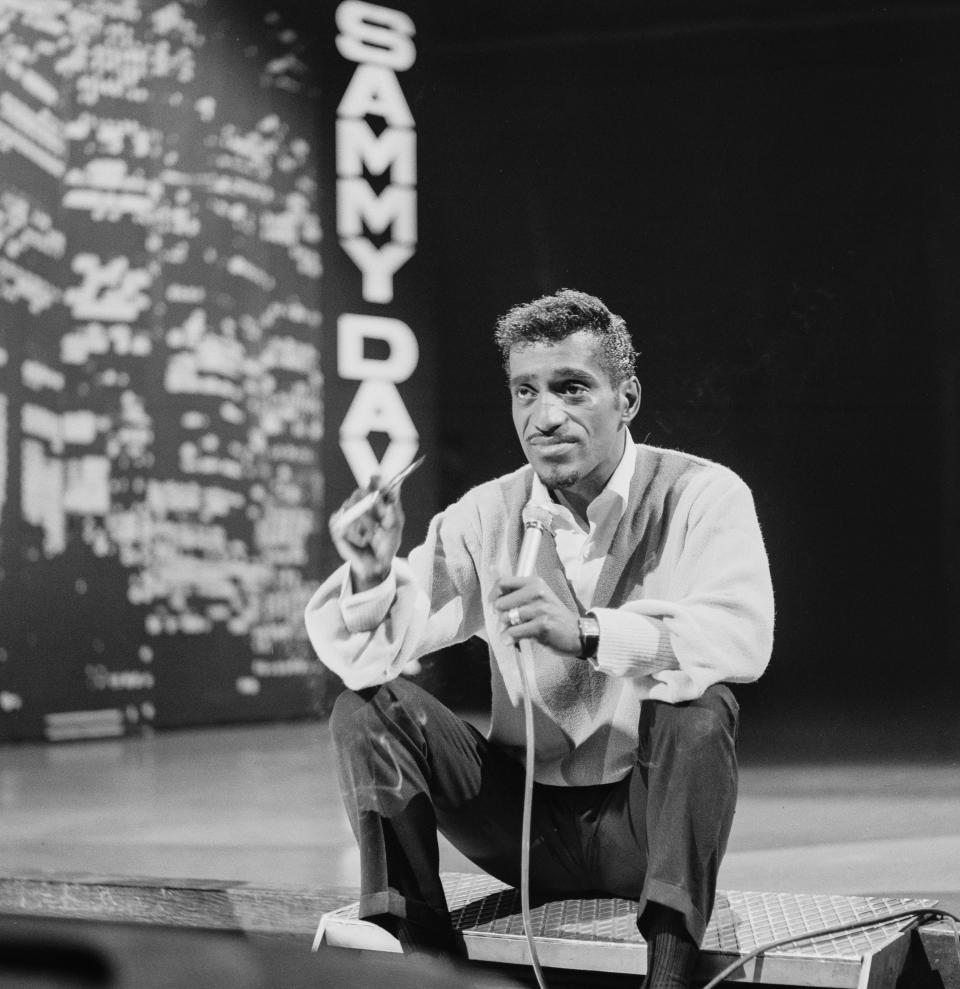 Sammy Davis Jr crouching on stage with a microphone