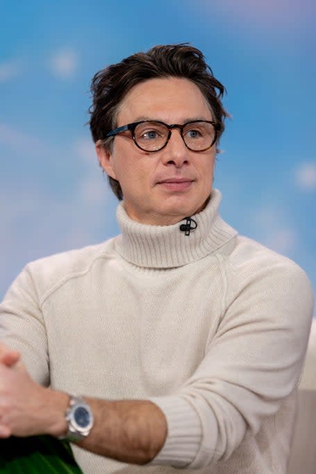 Man wearing glasses and a turtleneck sweater seated with crossed hands, interview setting with a blurred background