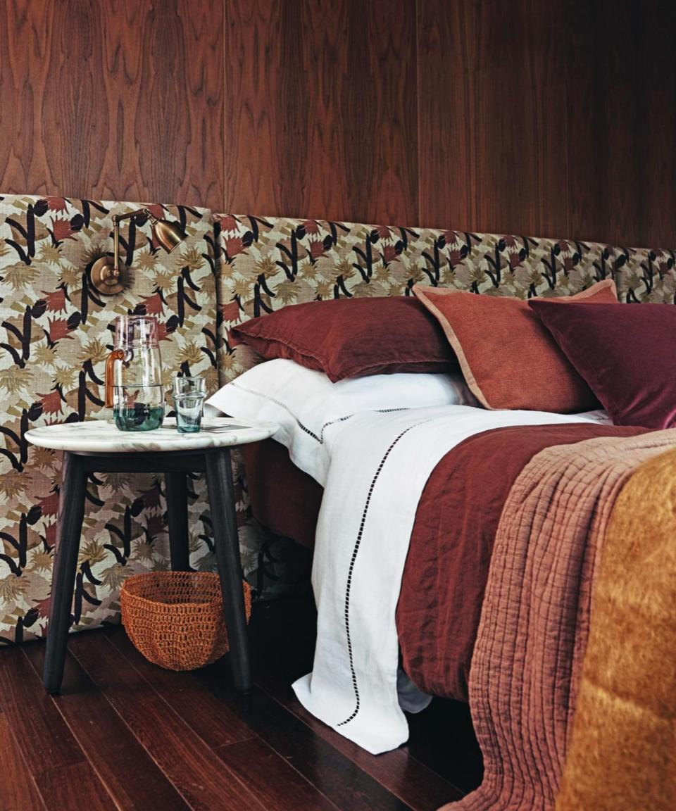 Bed in bedroom with feature headboard dressed in earthy tones and textured cushions.