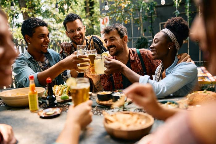 Group of friends sharing a meal outdoors, smiling and toasting with drinks