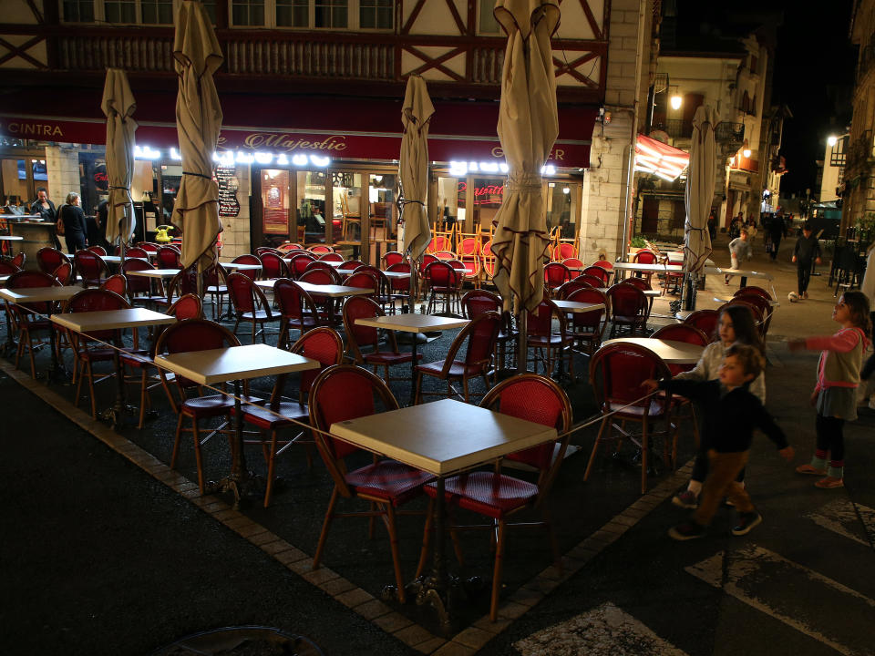 Children walk by a restaurant as it closes a few minutes before curfew in Saint Jean de Luz, southwestern France, Saturday, Oct. 24, 2020. A curfew intended to curb the spiraling spread of the coronavirus, has been imposed in many regions of France including Paris and its suburbs. (AP Photo/Bob Edme)