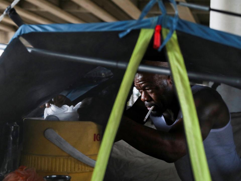 man in tent sweatign with cigarette reaches into cooler