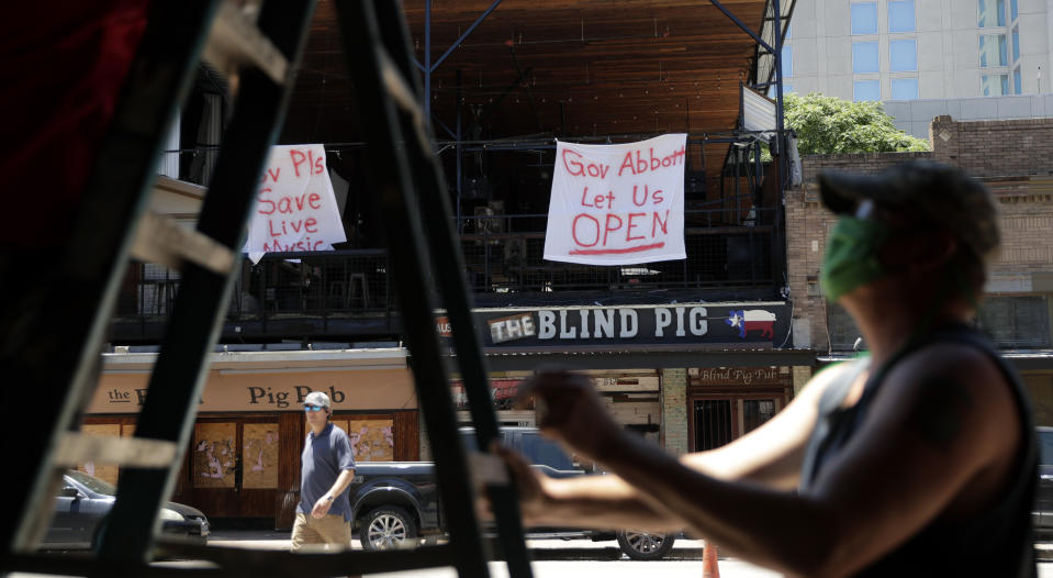 Signs directed at Texas Gov. Greg Abbott hang on a pub behind workers preparing another pub that they hope to reopen soon in Austin, Texas, Monday, May 18, 2020. Texas continues to go through phases as the state reopens after closing many non-essential businesses to help battle the spread of COVID-19. (AP Photo/Eric Gay)