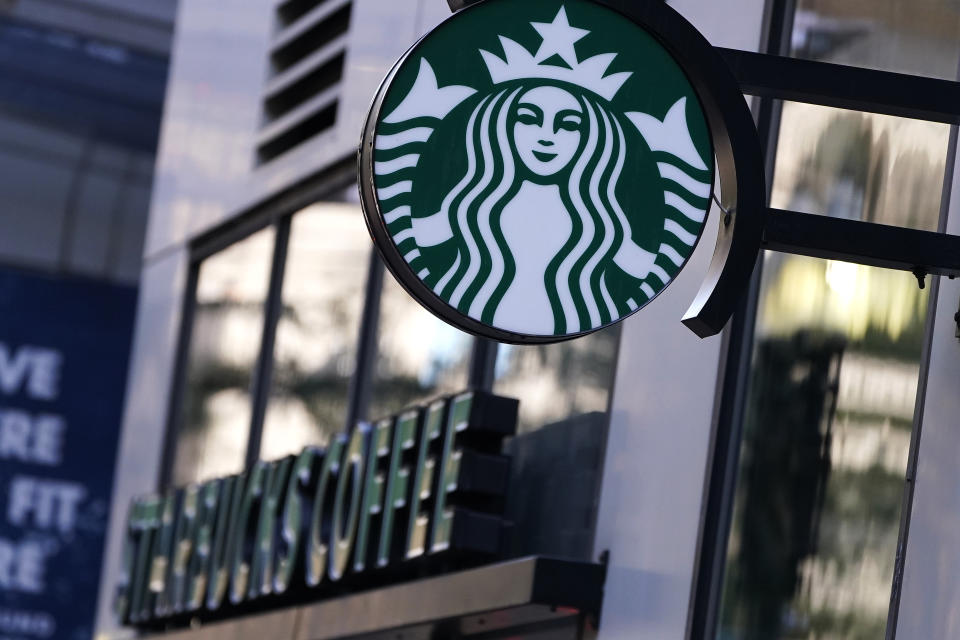 The "Siren" logo hangs outside a Starbucks Coffee shop, Wednesday, July 14, 2021, in Boston. Starbucks said Wednesday, Oct. 27 it is raising its U.S. employees’ pay and making other changes to improve working conditions in its stores. (AP Photo/Charles Krupa)